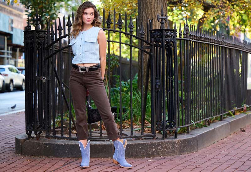 Woman standing in front of a black iron fence wearing a pair of Lea 9" Suede western boots in blue.